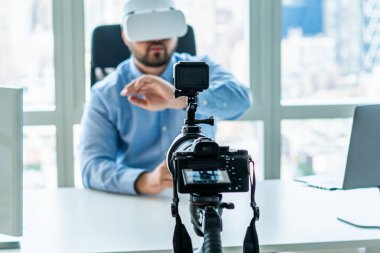 Modern kamera yetişkin bir adamı sanal gerçeklik teknolojisi kullanarak kaydediyor. Gözlük takıyor ve ofiste bilgisayar masasında çalışıyor.