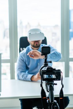 Modern kamera yetişkin bir adamı sanal gerçeklik teknolojisi kullanarak kaydediyor. Gözlük takıyor ve ofiste bilgisayar masasında çalışıyor.