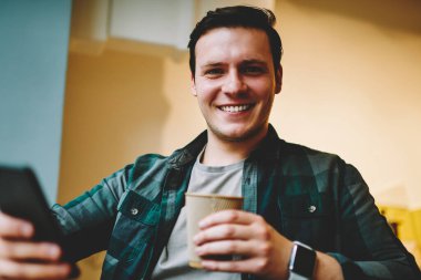 Neşeli genç adam ağ telefon, müreffeh erkek blogger takipçileri smartphone üzerinden sohbet için iyi Wi-Fi bağlantısı ile kafeteryada oturan eğlence üzerinde favori kahve zevk