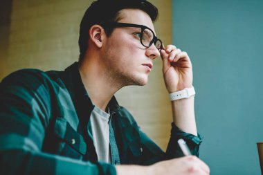 Akıllı genç hipster adam sorun çözüm coworking boşluk, notlar ve planlama kurs için yaratıcı fikir konsantre Eyewear düşünceli erkek öğrenci ödev hakkında düşünme