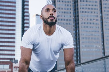 Sabahları eşofman ve eldiven giyen aktif sakallı vücut geliştiricilerden binaların arka planına bakmak için kalas egzersizi yapıyorlar.