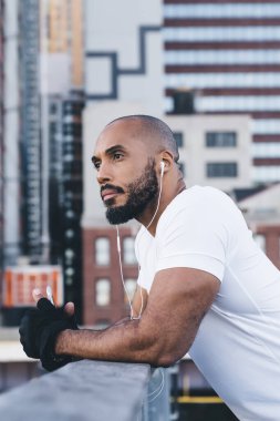 Düşünceli, kel, Afro-Amerikan sporcu kıyafetli, eğitime ara verilirken korkuluklara yaslanırken yüzünü çeviren Amerikalı sporcunun yan görüntüsü