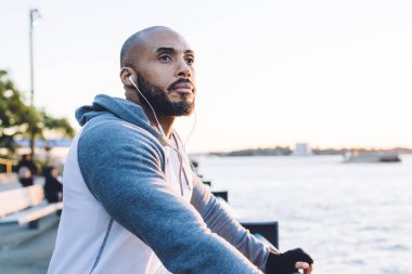 Kenar manzaralı, kulaklıklı, kentin kıyısındaki metal çitlerde duran kendine güvenen siyahi adam sabah vakti kararlılıkla başka tarafa bakıyor.