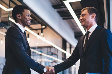 Dinlenme odasındaki neşeli, çoklu etnik çeşitliliğe sahip yakışıklı iş adamlarının düşük açılı görüşü, anlaşmaları gerçekleştirmek ve modern iş merkezinde el sıkışmak için uygun.