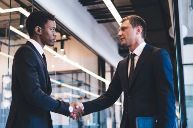 Dinlenme odasındaki çok ırklı girişimciler, modern ofis binasında cam duvarlar ve el sıkışarak bir anlaşma imzalarken,