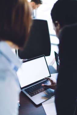 Ofiste ayakta durup yaslanırken dizüstü bilgisayar kullanan ve bilgi paylaşan çok ırklı çok ırklı iş arkadaşlarının arka görünümü