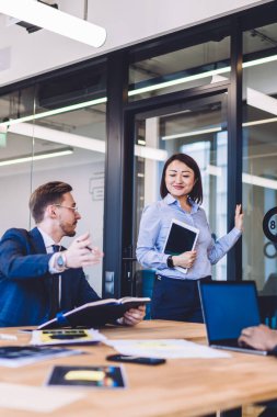 Çok yönlü başarılı insanlardan oluşan bir grup büyük açık ofiste klasik giyinmiş bir adam kapıdaki iş kadınının oturmasını öneriyor.