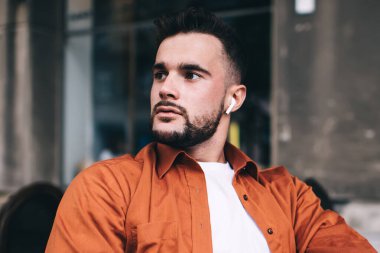 Yakışıklı, sıradan giyinen, dizüstü bilgisayarda çalışan ve kahve fincanı ile kafede otururken yüzünü çeviren bir erkek öğrenci.