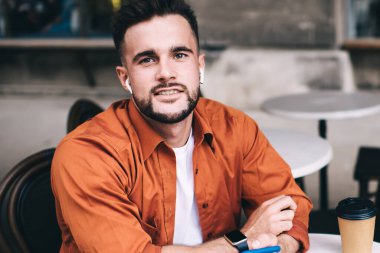 Mutlu ve neşeli bir adam kapalı dizüstü bilgisayarın önünde oturuyor ve sosyal medyaya bakıp gülümsüyor ve kameraya bakıyor.