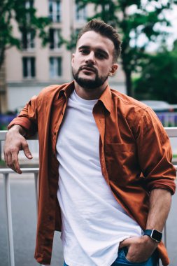 Kendine güvenen sakallı adam el ele tutuşup kameraya bakarken sokağın yakınındaki metal çitlere yaslanıyor.