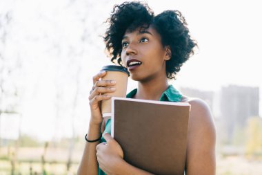 Çekici, siyah tenli, kıvırcık saçlı bir kadın açık havada kahve eşliğinde duran bir şeye hayran kalmış güzel, Afro-Amerikan hippi kız dışarıda sürpriz bir şekilde vakit geçirdiğini ifade ediyor.