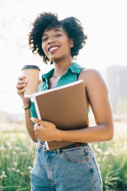 Güneşli bir günde kahve içmek için kıvırcık saçlı, esmer hippi kızın yarım boy portresi. Çekici Afrikalı Amerikalı kadın moladan ve boş zamanlardan zevk alıyor.