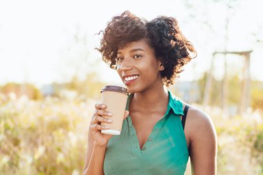 Başarılı koyu tenli, serbest çalışan bir kadın dizüstü bilgisayarda uzaktan çalışıyor güneşli bir günü açık havada geçiriyor, mutlu koyu tenli dijital göçebe kahve içip internet sitelerinde yayınlanıyor.