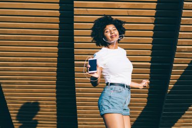 Neşeli, mutlu, Afro-Amerikan melodisi kulaklıklarla hoplayıp zıplayan, kaygısız, duygusal, koyu tenli hippi kız hafta sonları parkta şarkı listesi şarkıları eşliğinde dans ediyor.