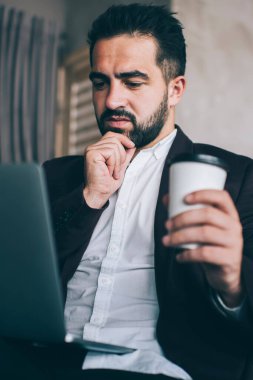 Düşünceli Kafkasyalı tüccar dizüstü bilgisayar kullanarak haberlere kafa yoruyor, düşünceli erkek yönetici finans raporunu internetten modern cihazlarla okudu.