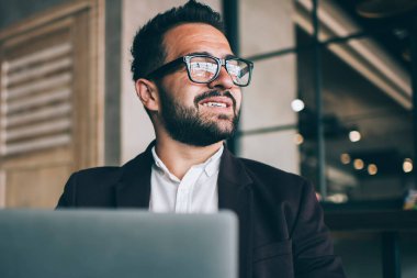 Gözlüklü başarılı beyaz erkek girişimci uzak bir iş için dizüstü bilgisayar kullanarak online projeden memnun. Mesafeli çalışma süresince gülen resmi giyimli mutlu iş adamı.