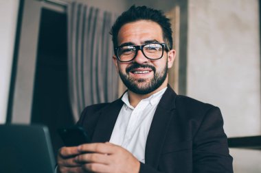 Modern cihazlar aracılığıyla serbest çalışmanın keyfini çıkaran neşeli erkek girişimci, başarılı iş adamı, cep telefonu hizmetinden memnun olan bankacılık uygulaması aracılığıyla çevrimiçi ödemeyi doğruladı