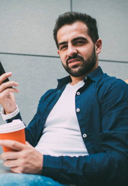 Sakallı, serbest çalışan, cep telefonuyla Fin Cafe 'de kahve içerek çalışan, ciddi beyaz erkek öğrenci bilgisayar ve 4G ile çevrimiçi kurslar öğreniyor.