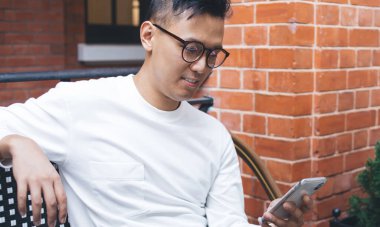 Ara verdiğimizde sokak kafeteryasında otururken, gözlüklü ve günlük giysileri olan mutlu Asyalı genç bir adam elinde telefonla oturuyordu.