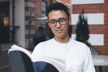 Şehir kafeteryasında tek başına oturup üniversite sınavlarına hazırlanırken büyük bir konsantrasyonla ilginç kitaplar okuyan Asyalı neşeli adam.