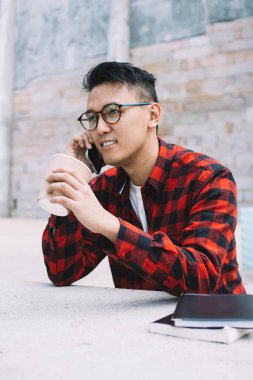 Gözlüklü, sıradan kıyafetleri olan, telefonla konuşan ve kahve içen düşünceli Asyalı serbest yazar. Gündüz vakti elinde not defteriyle taş masada oturuyor ve gözlerini kaçırıyordu.