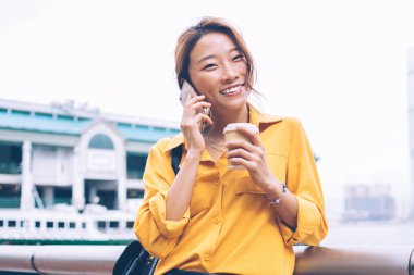 Sarı bluz ve siyah deri etek giyen güzel bir Asyalı kadın gülümsüyor ve cep telefonundan arıyor. Hong Kong 'da, feribot iskelesinde kahve alıyor.