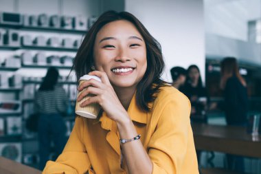 Gülümseyen Asyalı kız öğrenci, yemek arasında laptopuyla kahve içiyor ve Hong Kong 'daki elektronik mağazasında kameraya bakıyor.