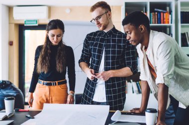 Tasarım projesinde işbirliği yapan çok kültürlü erkek ve kadın meslektaşlar plan çizimlerinde yaratıcılıkla beyin fırtınası yapıyorlar, milenyumlar birlikte çalışma alanında fikir alışverişinde bulunuyorlar.