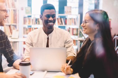 Çeşitli öğrencilerden oluşan bir grup kahve dükkanında oturuyor ve iş birliği yapmak ve kapalı alanda öğrenim görmek için gülüyor. Başarılı binyıllar boyunca fikirler tartışıyor ve üniversite kampüsünde masanın yanında gülümsüyor.