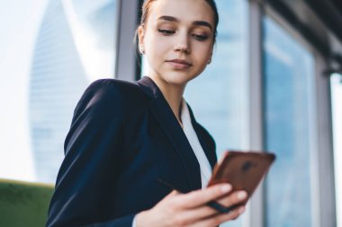 Ofis odasında koçun yanında otururken modern akıllı telefonu dikkatle kullanan resmi kıyafetli güzel bir bayan çalışana odaklanmış.