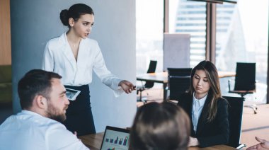 Kendine güveni tam bir yönetici kadın. Tableti elinde tutan ve masa başında çalışanlarla modern ofiste erkek işçilerle tartışıyor. Planları tartışıyorlar.