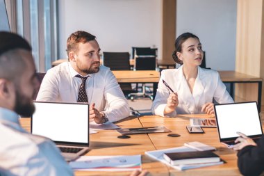 Resmi olarak odaklanmış ofis çalışanları, modern şehir ofisindeki belgelerle konferans masasında otururken projeyi tartışırken ve dizüstü bilgisayarda gezinirken,
