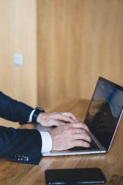 Ofiste otururken modern dizüstü bilgisayarın klavyesinde yazan koyu takım elbiseli anonim girişimcinin yan görüntüsü