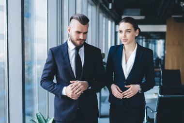 Şık takım elbiseli ciddi moda iş arkadaşları panoramik pencerenin yanında yürüyor ve Megapolis 'teki hafif ofiste iş planlarını tartışıyorlar.