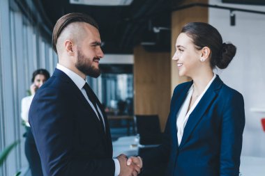 İş dünyasındaki modaya uyan girişimcilerin yan görüşü açık alan modern minimalist ofiste anlaşma sağlamakta ve birbirine bulanık arka planda bakmakta.