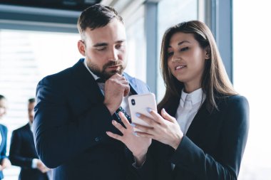 Takım elbiseli mutlu bir kadın, şehir konferans odasının penceresinin yanında resmi giyinmiş, akıllı telefon kullanıyor.