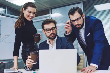 Mutlu resmi iş ekibi kahve içiyor ve internet üzerinden sohbet etmek için iş yerinde dinleniyor. Gözlüklü adam, meslektaşlarına son sunumlarının videosunu modern laptopta gösteriyor.