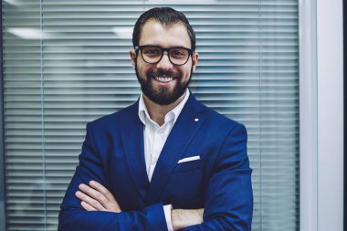 Şık takım elbiseli, kendine güvenen, şık takım elbiseli, ofis şirketinde çalışırken kameraya bakan ve gülümseyen mutlu yönetmen portresi göz koruması sağlamak için optik gözlük takan mutlu yönetmen.