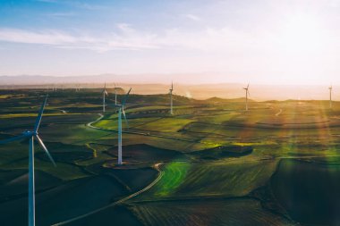 Turuncu günbatımı gökyüzü üzerinde kırsal tarım arazisi tarım çayırında duran dönen pervaneler ile modern yel değirmenleri. Temiz kaynaklar için yenilenebilir enerji üreten rüzgar üfleme. Elektrik enerjisi üretimi