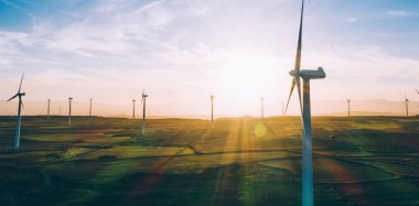 Turuncu günbatımı gökyüzü üzerinde kırsal tarım arazisi tarım çayırında duran dönen pervaneler ile modern yel değirmenleri. Temiz kaynaklar için yenilenebilir enerji üreten rüzgar üfleme. Elektrik enerjisi üretimi