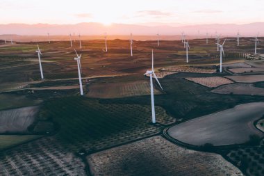 Turuncu günbatımı gökyüzü üzerinde kırsal tarım arazisi tarım çayırında duran dönen pervaneler ile modern yel değirmenleri. Temiz kaynaklar için yenilenebilir enerji üreten rüzgar üfleme. Elektrik enerjisi üretimi
