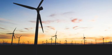 Mavi günbatımı gökyüzüne karşı kırsal tarım ortamında Eko kaynaklardan alternatif temiz yeşil güç üreten pervaneler ile yel değirmenleri İstasyonu silueti. Elektrik üreten türbinlerin çiftliği