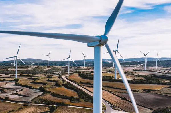 Kırsal tarım ortamında eko kaynaklarından alternatif temiz yeşil enerji üreten dönen pervaneli yel değirmenlerinin hava görüntüsü. Kuş bakışı türbinlerin elektrik üreten hattına bakıyor.