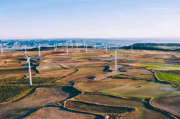 Kırsal tarım ortamında eko kaynaklarından alternatif temiz yeşil enerji üreten dönen pervaneli yel değirmenlerinin hava görüntüsü. Kuş bakışı türbinlerin elektrik üreten hattına bakıyor.