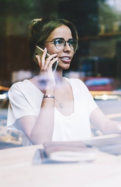 Dizüstü bilgisayar üzerinde çalışma kursu çalışma sırasında dostu hücresel çağrı zevk pozitif hipster kız, Netbook ile oturan gözlük mutlu kadın ve mobil gadget App aracılığıyla meslektaşım ile konuşurken