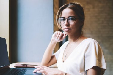 Uzaktan çalışan çekici kadın programcı portresi ve yeni Web sitesi oluşturma break kamera bakıyor, yeni modern Netbook ile masada oturan optik gözlük güzel yetenekli kadın