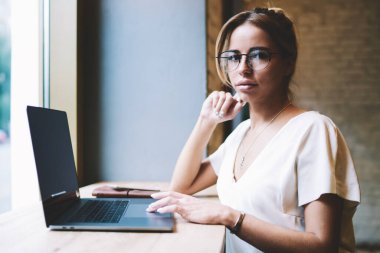 Uzaktan çalışan çekici kadın programcı portresi ve yeni Web sitesi oluşturma break kamera bakıyor, yeni modern Netbook ile masada oturan optik gözlük güzel yetenekli kadın