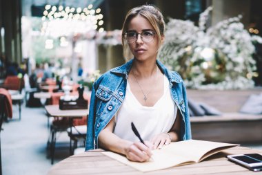 Rahat iç, özenli hipster kız optik gözlük uzağa bakarak ve proje hakkında düşünme ile kafeterya otururken Restoran hakkında blog için yeni makale üzerinde durulması Pensive kadın