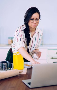 Güzel ve kendine güvenen bir kadın mutfakta duruyor ve sağlıklı yemek tarifi ararken sosyal medyada geziniyor.