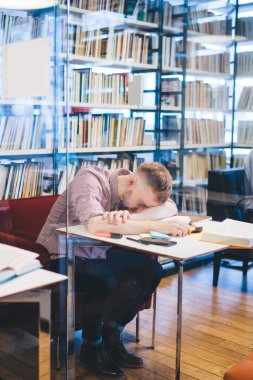 Odaklanmış çok ırklı yöneticiler resmi giysiler içinde cihazlara bakıyorlar ve kütüphanede yüzüstü yatan yorgun meslektaşlarının yanında kitaplar okuyorlar.